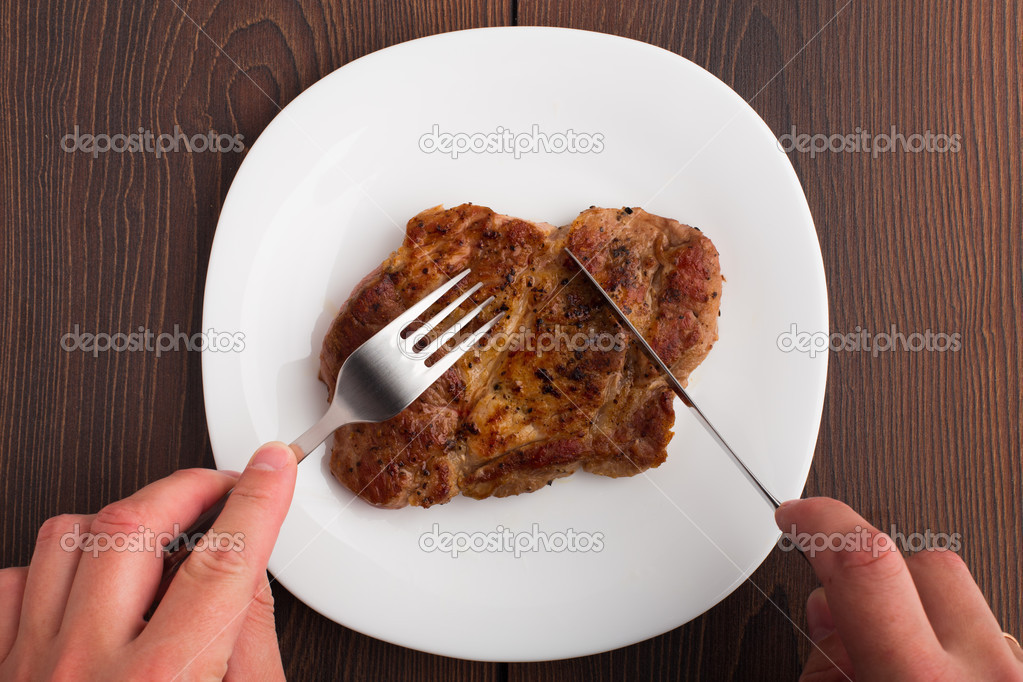 Someone eating grilled steak on white plate