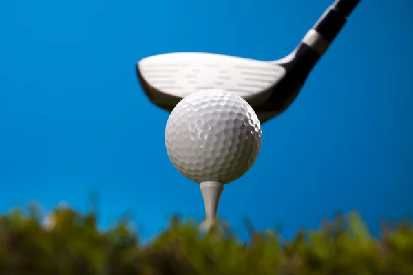 Bola de golfe na grama verde sobre um fundo azul — Fotografia de Stock