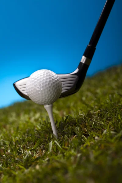 Bola de golfe na grama verde sobre um fundo azul — Fotografia de Stock