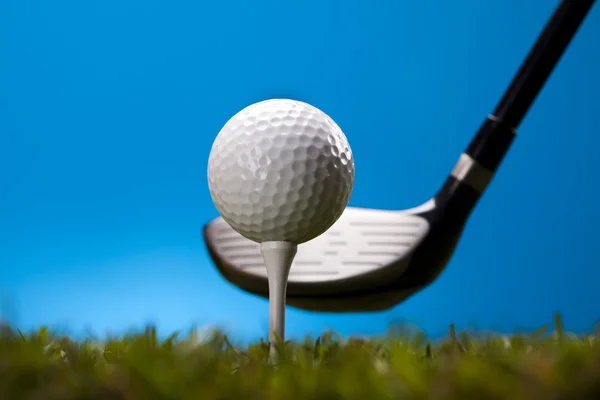 Bola de golfe na grama verde sobre um fundo azul — Fotografia de Stock