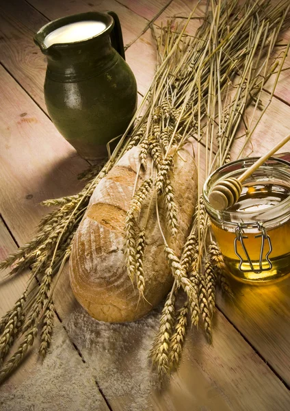 Буханка хлеба, кувшин молока и мёд на деревянном столе — стоковое фото