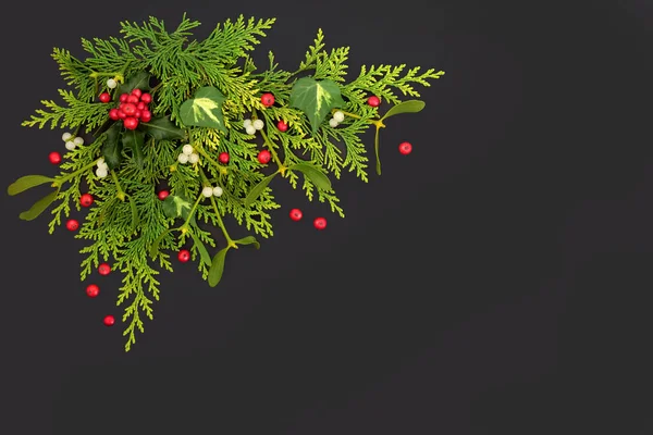 Holly, cedar, mistletoe, ivy leaves with red berries. Abstract nature Christmas background border for the winter solstice and Xmas festive season on dark grey. Flat lay.