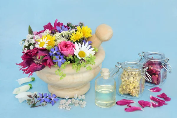 Herbs and flowers for herbal plant medicine and flower remedies in a mortar with aromatherapy oil. Used in essential oil aromatherapy treatments. Natural health care concept. On mottled blue.