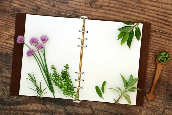 Recipe book with open pages and fresh kitchen garden herbs used in food seasoning and herbal plant medicine on rustic wood background. Flat lay, top view, copy space.