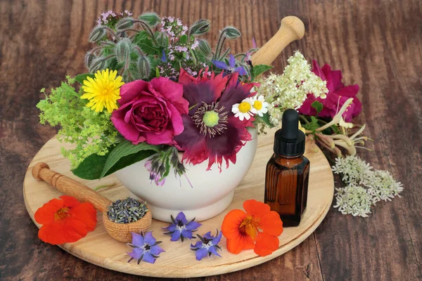 Herbs and flowers for alternative healing herbal medicine and flower remedies in a mortar with essential oil bottle. Natural health and wellness concept. On wooden board and rustic wood.