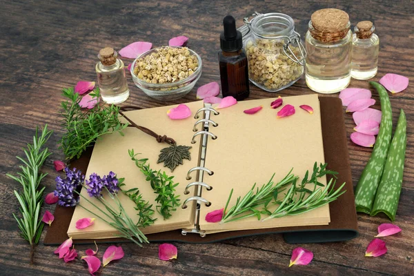 Natural herbal plant based medicine with herbs and flowers for plant based skincare remedies with essential oil bottles, old leather notebook for recipes and notes. On rustic wood background.