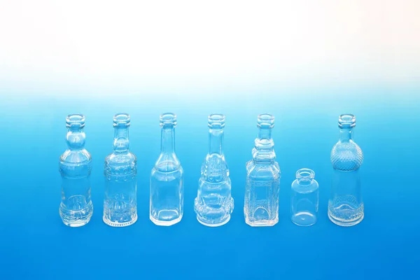 Odd one out concept with line of old retro glass bottles with one smaller in size. Minimal individuality composition on gradient blue white background.