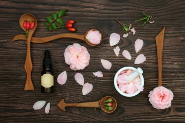 Rose flowers for aromatherapy essential oil preparation and rosehips for natural herbal plant medicine. Natural alternative edible flora for food decoration. On rustic wood.