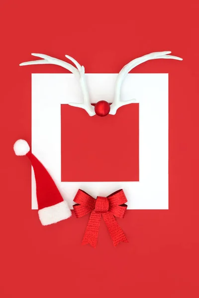 Christmas santa hat with reindeer antlers, gift bow on red background with white frame border. Traditional  festive symbols for the holiday season.