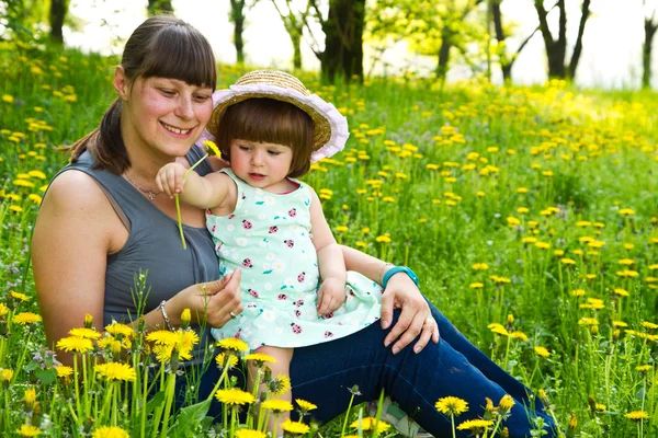 Moeder en kind ruiken een bloem op lente veld — Stockfoto