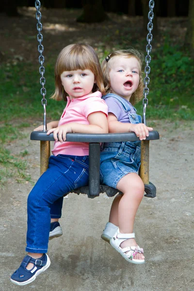Meninas pequenas felizes balançando em um parque — Fotografia de Stock