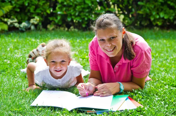 Happy mother drawing a book with baby girl in garden — Stock Photo, Image