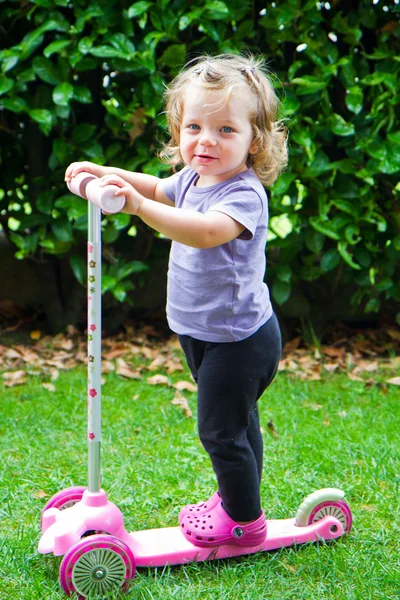 Bebê menina equitação no jardim em scooter — Fotografia de Stock