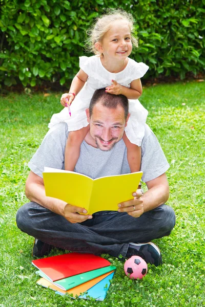 Vater liest seiner Tochter ein Buch vor, während sie im Garten im Gras liegt — Stockfoto