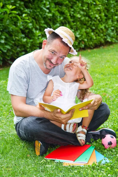 Vater liest seiner Tochter ein Buch vor, während sie im Garten im Gras liegt — Stockfoto