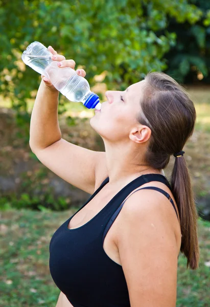 Retrato de jovem mulher bebendo água contra um fundo de plantas — Fotografia de Stock