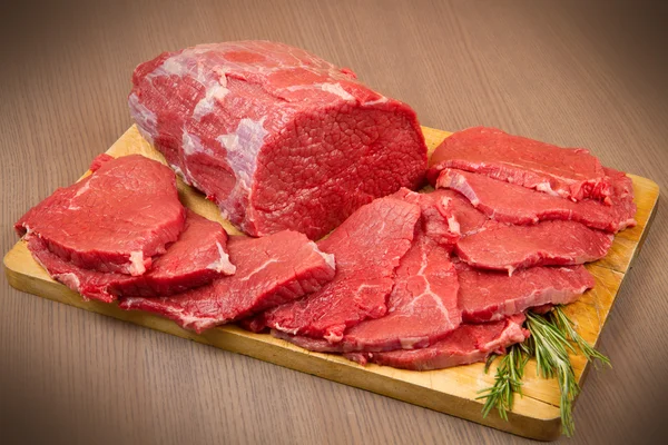 Huge red meat chunk and steak on wood table — Stock Photo, Image