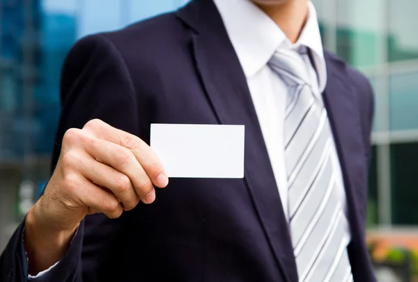 Young businessman holding visit card in hand and standing in the — Stock Photo, Image