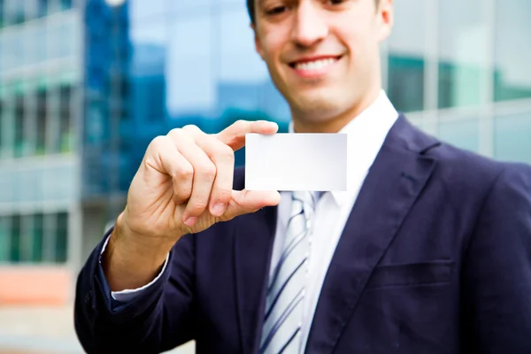 Young businessman holding visit card in hand and standing in the — Stock Photo, Image