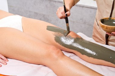 relaxing woman lying on a massage table receiving a mud treatmen clipart