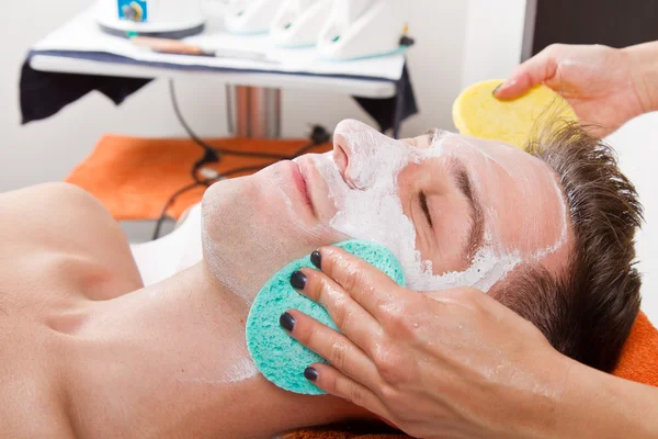 Therapeut een gezichtsmasker toe te passen op een mooie jonge man in een spa — Stockfoto
