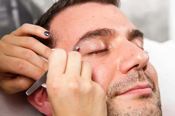 Esteticista arrancando un hermoso hombre cejas con pinzas en un —  Fotos de Stock