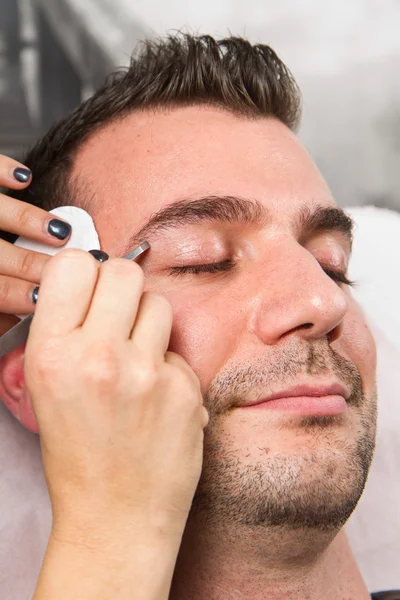 Kosmetikerin zupft einem schönen Mann mit einer Pinzette die Augenbrauen — Stockfoto