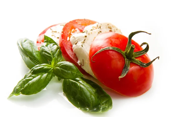 Tomaten und Mozzarella mit Basilikumblättern auf weiß — Stockfoto