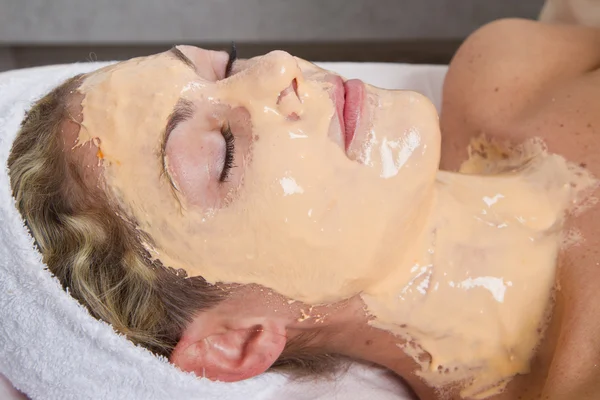 Therapist applying a face mask to a beautiful young woman in a s — Stock Photo, Image