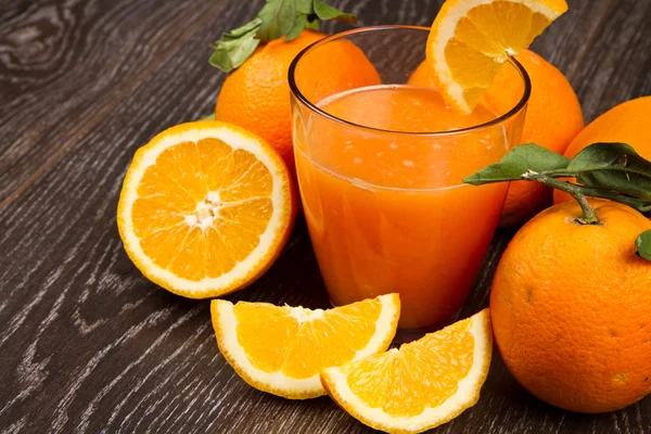 Verre de jus d'orange frais et d'oranges sur fond en bois — Photo