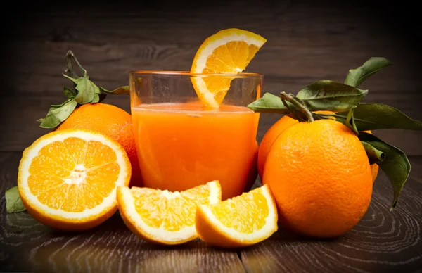 Sklenice čerstvé pomerančové šťávy a pomeranče na dřevěné pozadí — Stock fotografie