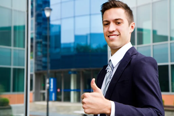 Молодой улыбающийся уверенный человек делает большие пальцы вверх вывеску за пределами офиса — стоковое фото