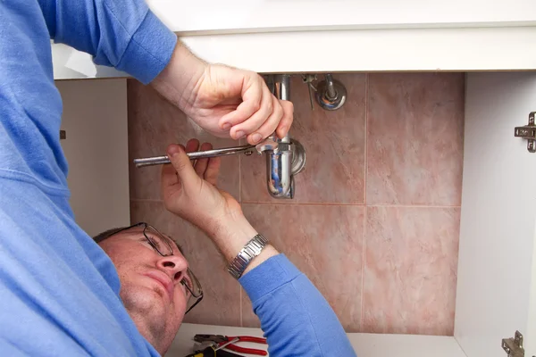 A plumber repairing a broken sink in bathroom — Stock Photo, Image