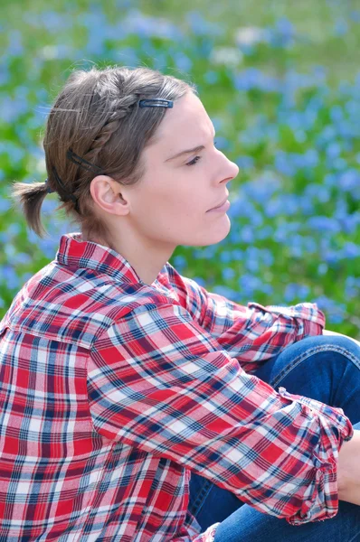 Jovem mulher atraente sentada em um prado com flor Scilla bifolia na primavera — Fotografia de Stock