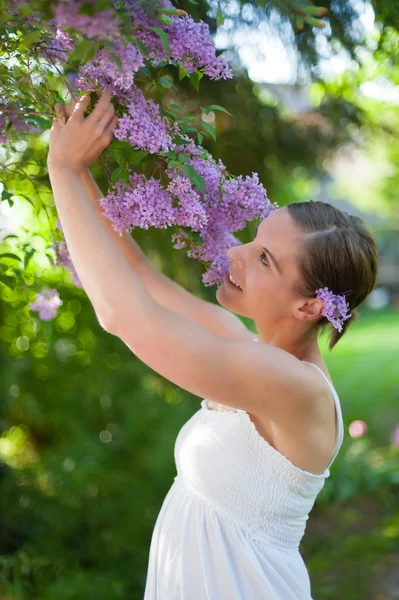 Jovem mulher gosta da fragrância de floração lilás — Fotografia de Stock
