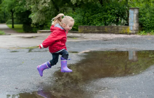 Menina bonito pulando sobre uma poça Imagens Royalty-Free