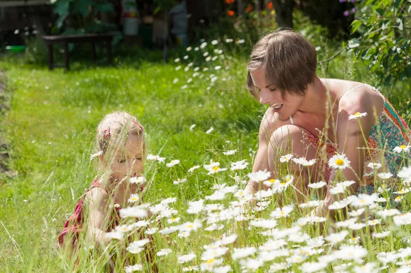 Mamma och hennes lilla dotter plockar blommor i en trädgård — Stockfoto