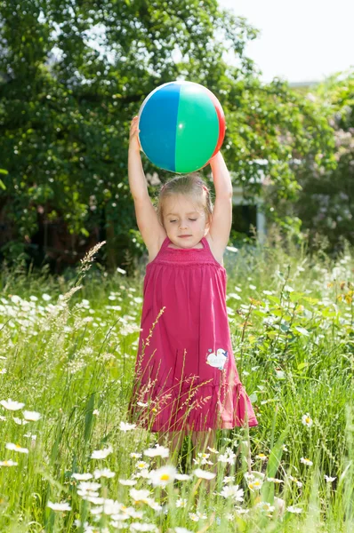 Malá dívka si hraje s míčem v kvetoucí zahradě — Stock fotografie