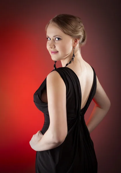 Mooi meisje in zwarte jurk op rode achtergrond — Stockfoto