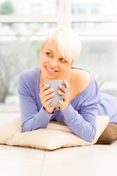 Pretty woman with mug on the floor laying on a pillow — Stock Photo, Image