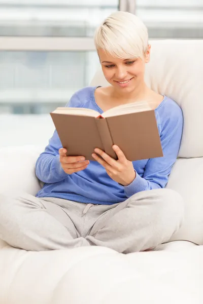 Lächelnde Frau entspannt sich beim Lesen eines Buches auf dem Sofa — Stockfoto