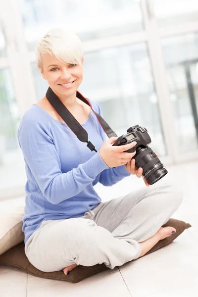 Vrouwelijke fotograaf met dslr thuis zittend op de vloer — Stockfoto