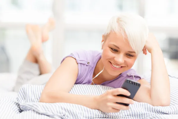 Young woman phoning in the bed with headphones — Stock Photo, Image