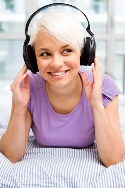 Mujer rubia escuchando música con auriculares en la cama — Foto de Stock