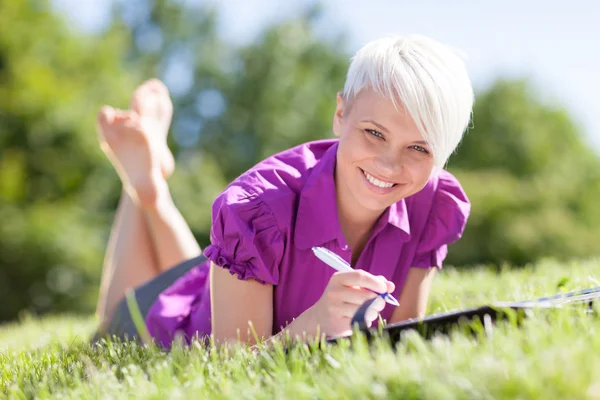 Hermosa estudiante femenina está estudiando en un campo verde —  Fotos de Stock