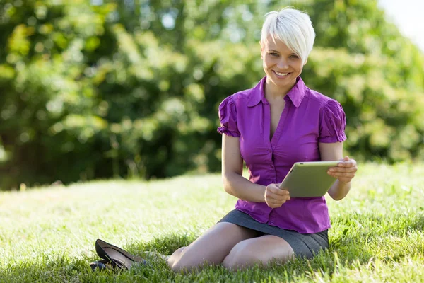 Lachende vrouw met tablet pc zit op het gras terwijl smili — Stockfoto