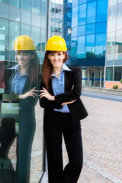 Consructor femenino sonriente junto a un edificio de vidrio — Foto de Stock