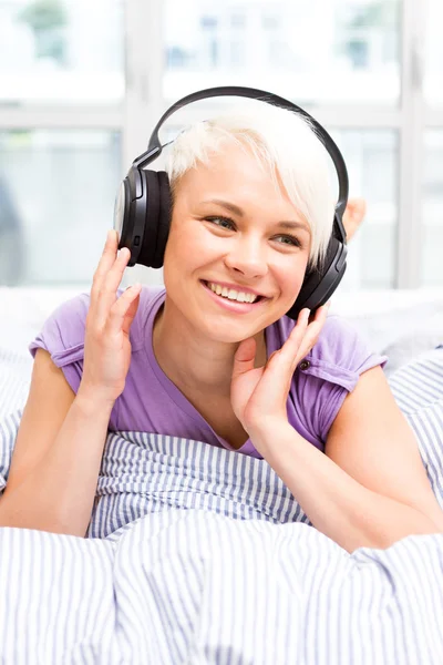 Mulher loira ouvindo música com fones de ouvido na cama — Fotografia de Stock