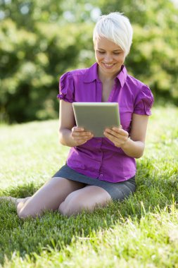 tablet pc ile gülümseyen kadın smili ise çimenlerin üzerinde oturuyor