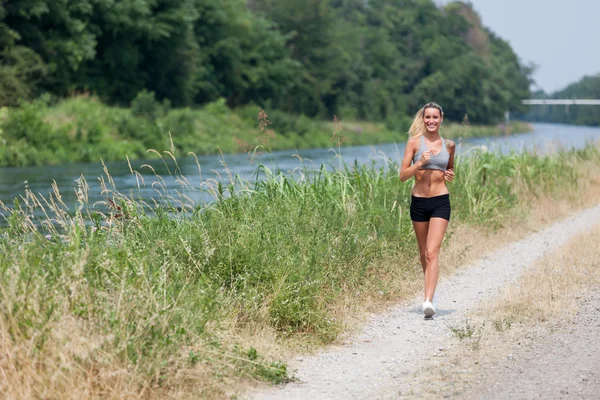 Beautiful blonde woman running along the riverside — Stock Photo, Image